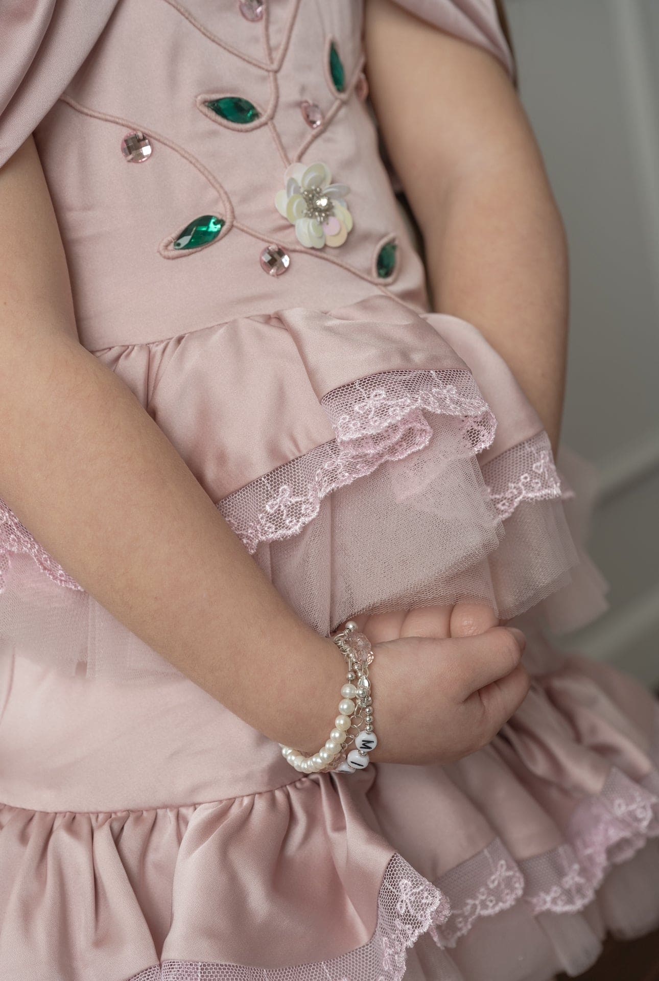 Close up of the pink satin ballerina dress showing jewel embellishments, delicate stitching, and soft satin texture