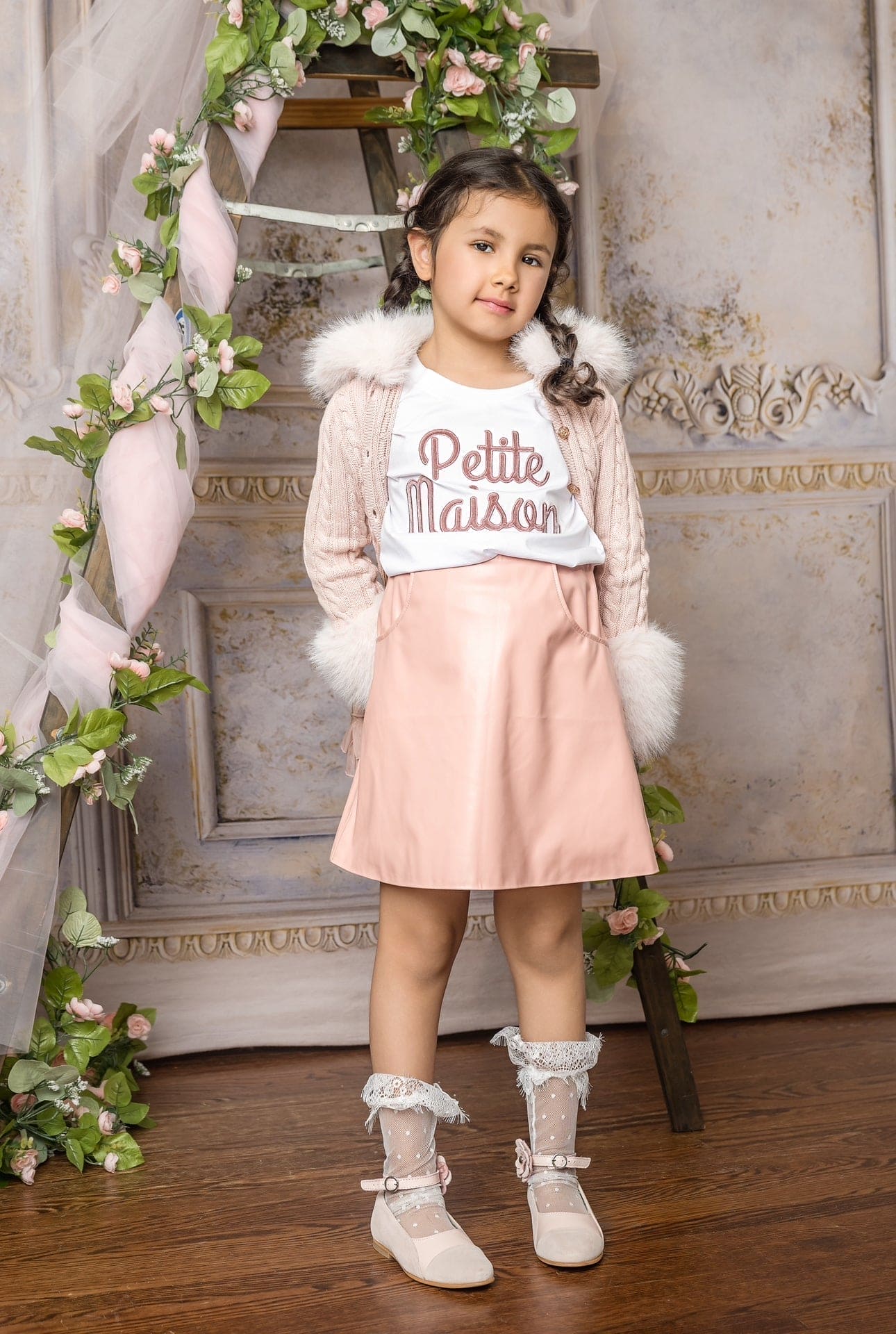 Girl wearing a pink vegan leather skirt featuring a soft faux leather texture, front pockets, and tailored above the knee fit