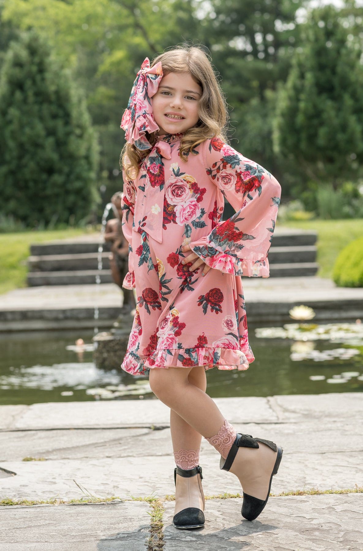 Girl wearing Flora flower print jumpsuit in pink floral design styled outdoors by a garden pond