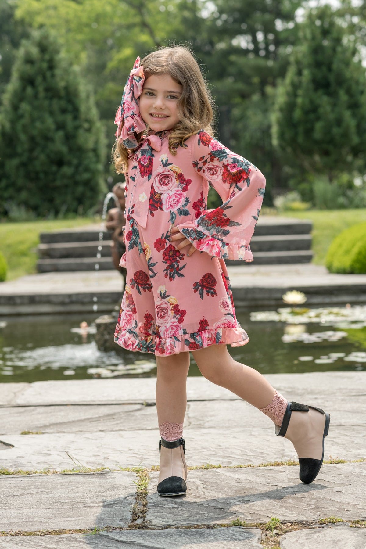 Flora flower print jumpsuit styled on a young girl with long sleeves and ruffle hem in pink floral fabric