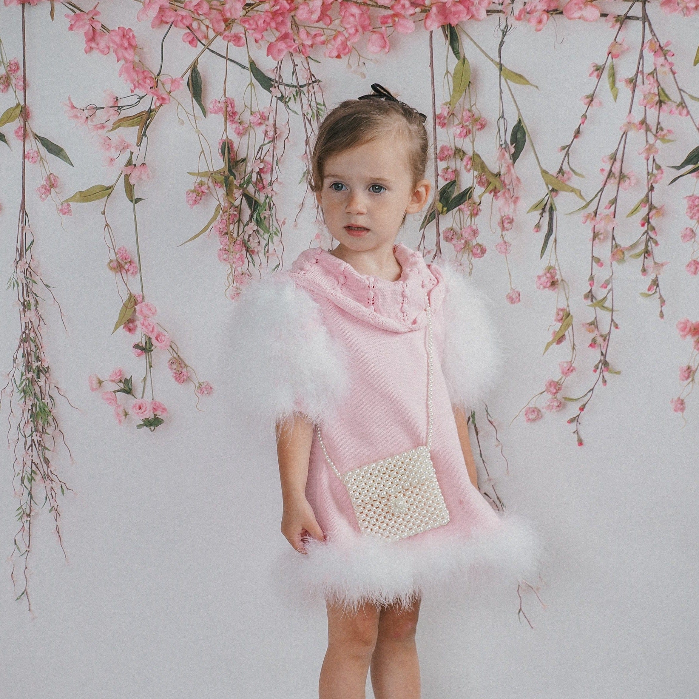 Young girl wearing Ella Knit pink dress featuring feather sleeves and embroidered neckline detail