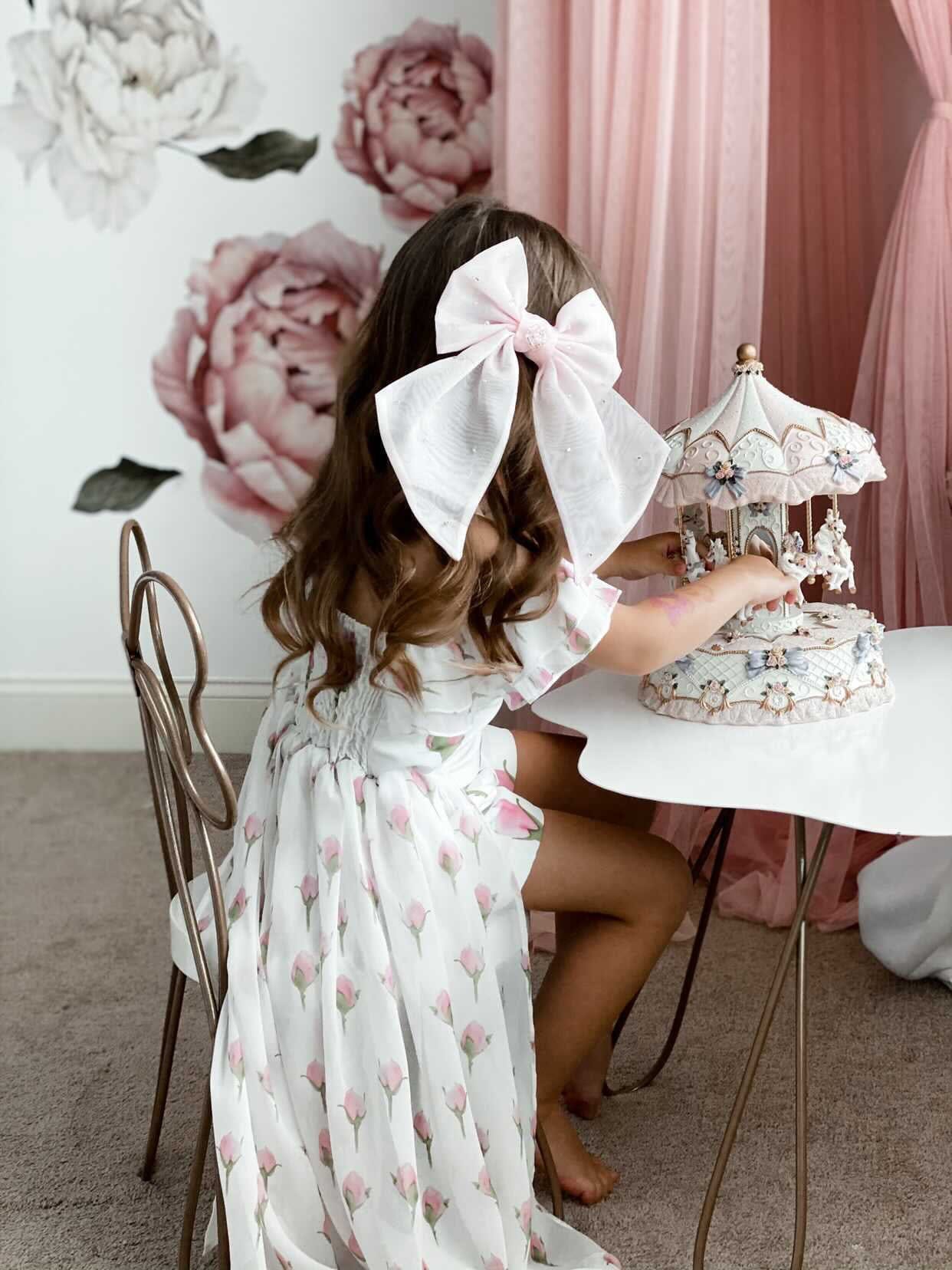 Young girl playing at table wearing the Juliette Pink Organza Hair Bow styled with a floral dress for a birthday photoshoot.