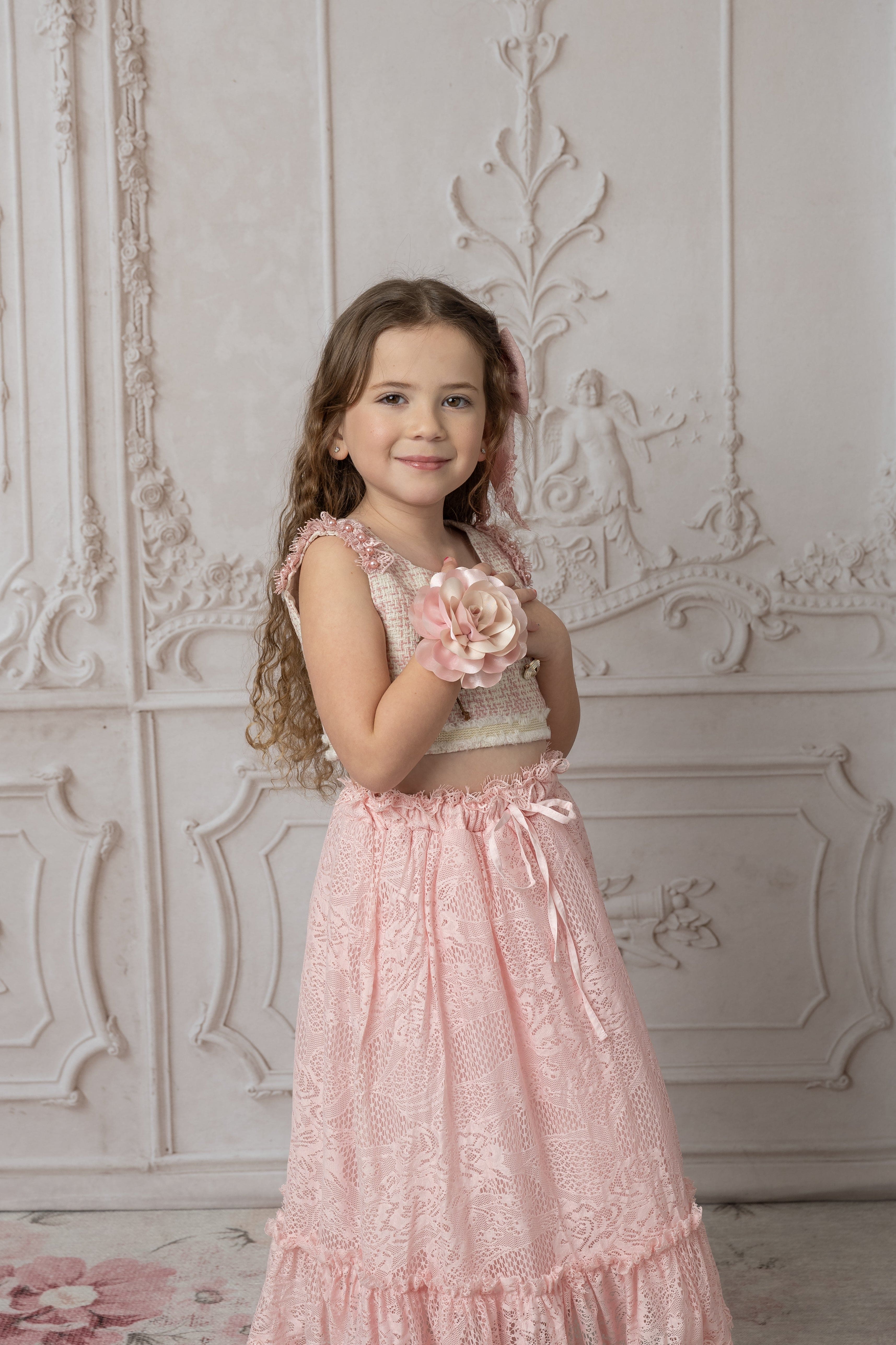 Girl wearing a beige and pink tweed top with a floral bracelet and pink lace skirt 