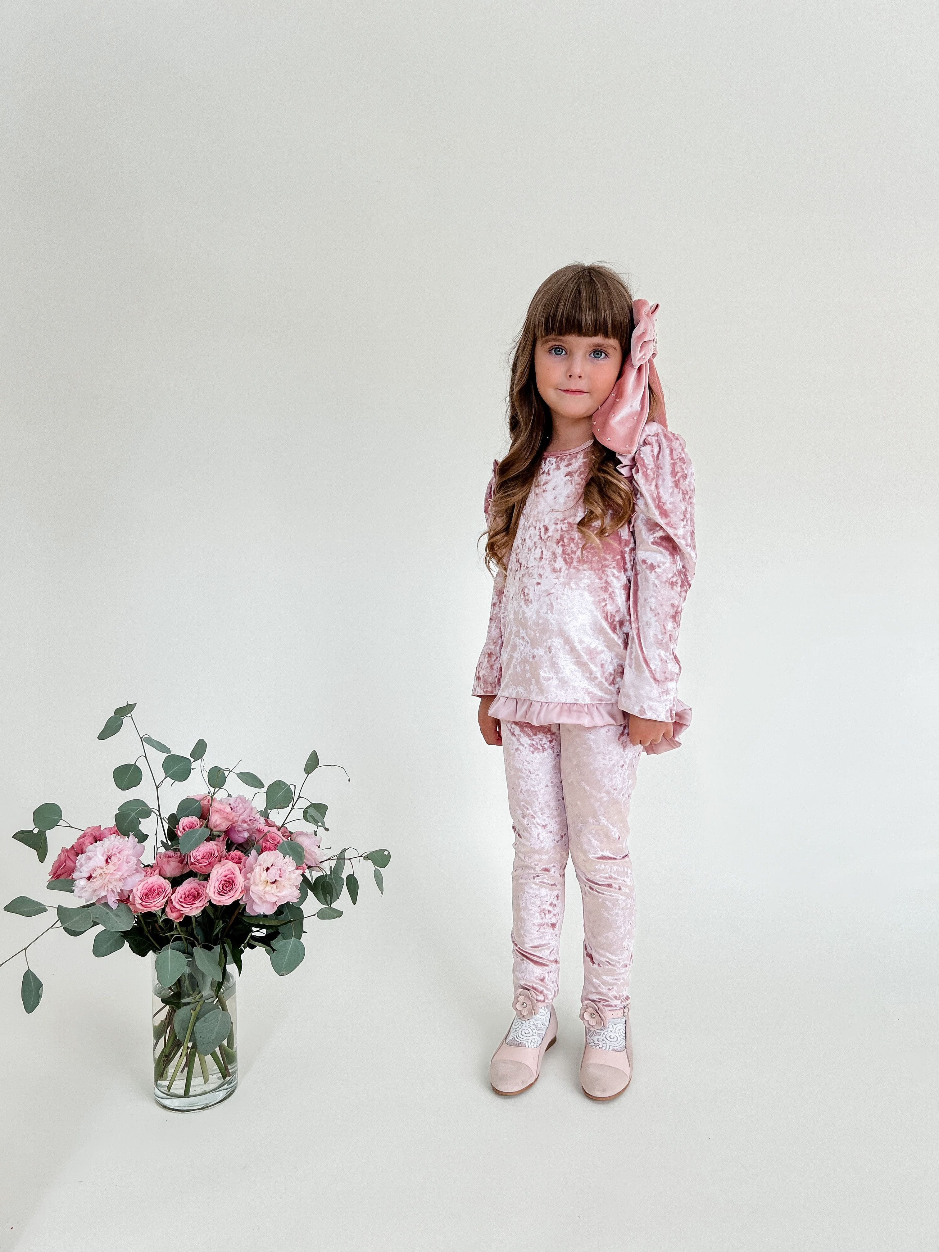 Girl modeling pink velour lounge set with oversized bow accessory and matching leggings