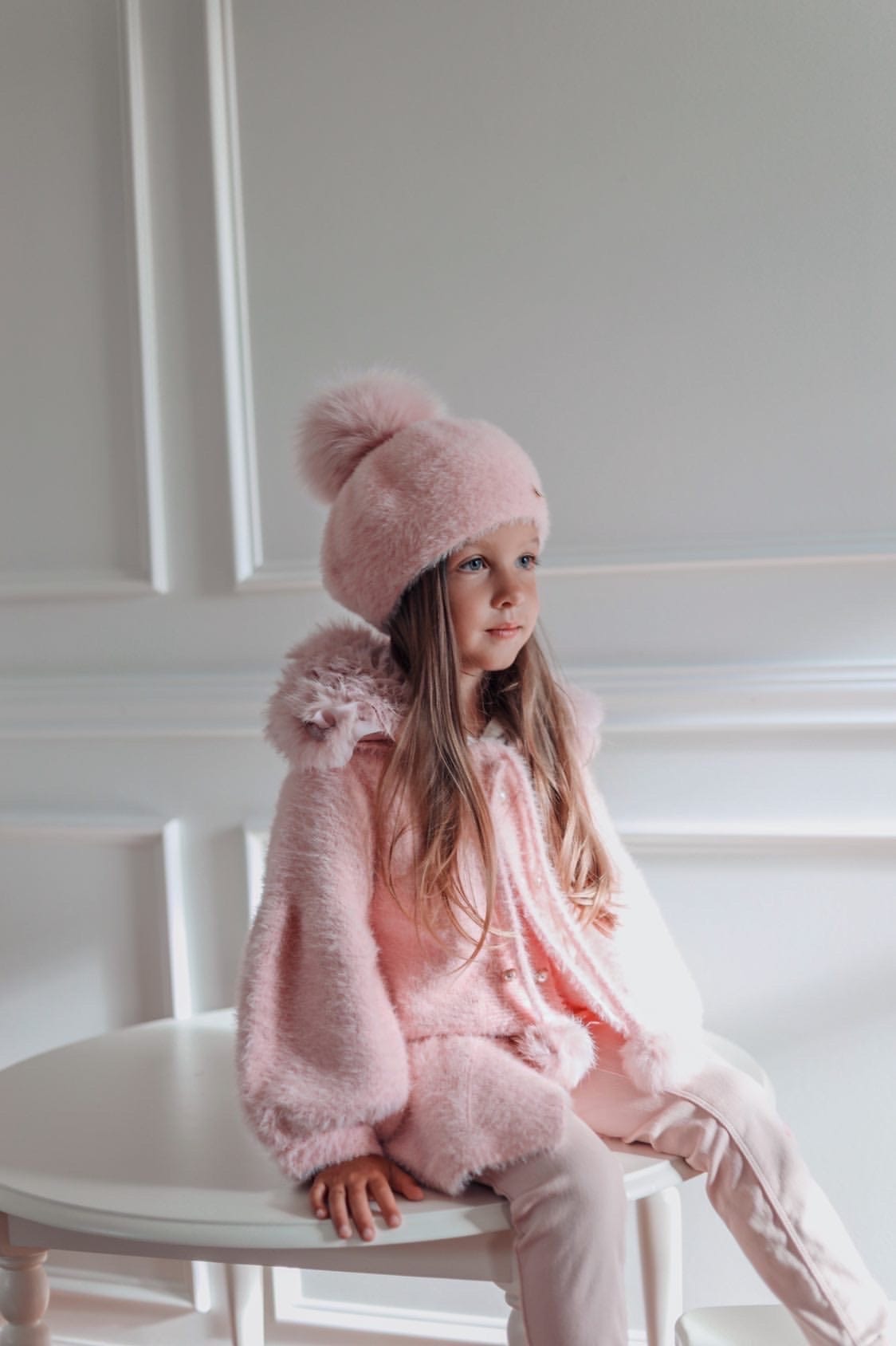 Girl sitting on white bench wearing Milana Rose Beret styled with matching pink faux fur coat and winter outfit.